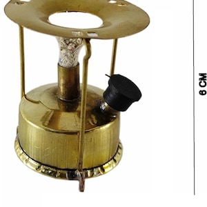 May include: A brass-colored camping stove, 5 cm wide and 6 cm tall, with a round top and a fuel tank. The stove has a black knob and a wick. The stove is designed for outdoor cooking and camping.