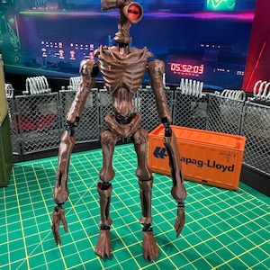 Könnte beinhalten: Eine braune, bewegliche Actionfigur mit einem großen, dünnen, skelettartigen Körper, langen Armen und einem Kopf aus zwei megaphonartigen Sirenen, von denen eine ein leuchtend rotes Zentrum hat. Die Figur steht auf einer grünen Rasterfläche.