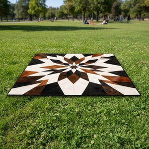 May include: A geometric patterned rug with a starburst design. The rug features a combination of black, white, and brown shapes. The rug is rectangular and is placed on a green grassy surface.