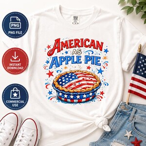 May include: White t-shirt with the text "AMERICAN AS APPLE PIE" in red and blue. The design features a pie with an American flag on top, surrounded by stars and fireworks. The shirt is paired with denim shorts and a small American flag.