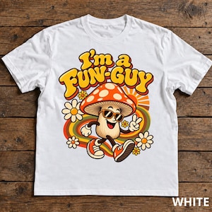 Op de afbeelding: Een wit t-shirt met een afbeelding van een lachende paddenstoel met een zonnebril en sneakers, die een vredesteken maakt. De tekst "I'm a FUN-GUY" staat erboven, omringd door kleurrijke bloemen en golvende lijnen.