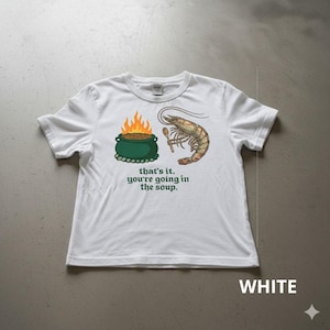 May include: White t-shirt with a humorous graphic. The design features a green pot with flames, a shrimp holding a spoon, and the text "that's it. you're going in the soup."