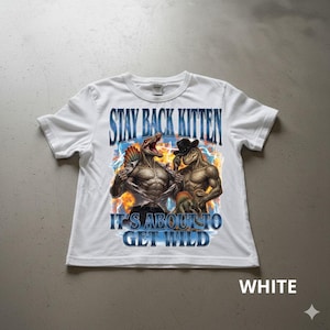 Puede incluir: Camiseta blanca con un gráfico de dos dinosaurios musculosos, uno rasgando su camisa. El texto dice "STAY BACK KITTEN" y "IT'S ABOUT TO GET WILD". La palabra "WHITE" está en la parte inferior.