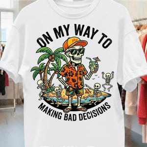 Op de afbeelding: Wit t-shirt met een afbeelding van een skelet met een zonnebril, een oranje hoed en een Hawaiiaans shirt, met een cocktail in de hand. De tekst luidt: "ON MY WAY TO MAKING BAD DECISIONS".