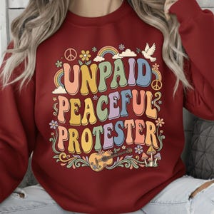 Może przedstawiać: Biały ceramiczny kubek z czarnym uchwytem i napisem "But First, Coffee" pogrubioną, czarną czcionką. Kubek jest ustawiony na rozmytym tle, sugerującym przytulne otoczenie.