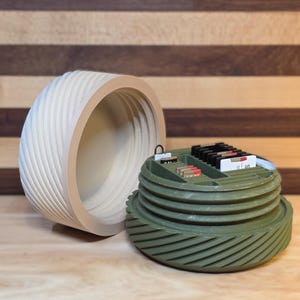 May include: A two-part container with a light wood-colored lid and a green base. The lid has a spiral design, and the base has a threaded, ridged exterior. The base is open, revealing small compartments holding various items.