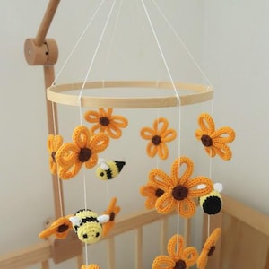 May include: A handmade baby mobile featuring crocheted yellow flowers with brown centers and adorable bee figures. The mobile is suspended from a wooden hoop and arm, creating a charming nursery decoration.
