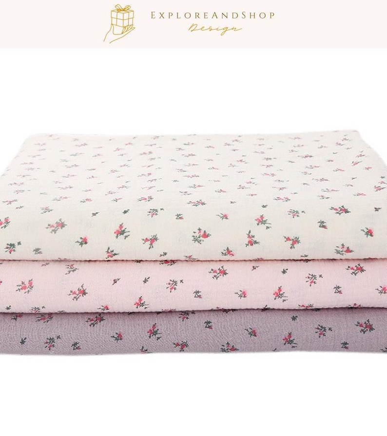 May include: Three folded fabric layers in cream, pink, and lavender, each adorned with a delicate floral pattern in red and green. The top layer is cream, the middle is pink, and the bottom is lavender. The image includes the text "EXPLOREANDSHOP Design".