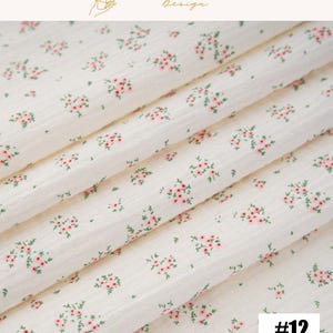 May include: Off-white fabric with a delicate floral pattern of small pink flowers and green leaves. The fabric is folded, showing the texture and design. The number "#12" is in the bottom right corner. The top of the image has the text "EXPLOREANDSHOP Design".