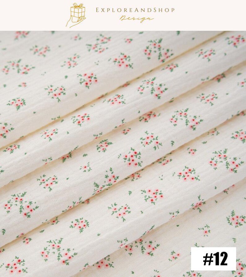 May include: Off-white fabric with a delicate floral pattern of small pink flowers and green leaves. The fabric is folded, showing the texture and design. The number "#12" is in the bottom right corner. The top of the image has the text "EXPLOREANDSHOP Design".