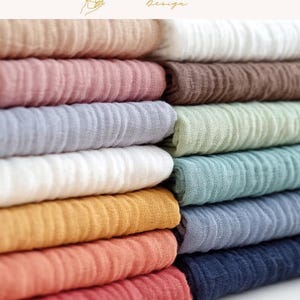May include: A stack of folded fabric in various colors, including beige, pink, brown, gray, green, blue, white, yellow, orange, and red. The fabric has a textured, crinkled appearance. The top right corner of the image has the text "EXPLOREANDSHOP Design".