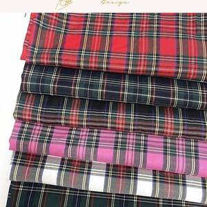 May include: A stack of folded fabric pieces featuring various plaid patterns in red, dark green, black, pink, white, and tan. Each piece displays a woven tartan design with intersecting horizontal and vertical lines of contrasting colors.