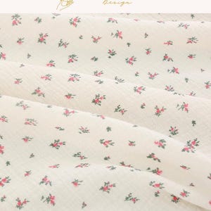 May include: Close-up of a cream-colored fabric with a delicate floral pattern. Tiny red and green floral clusters are scattered across the surface. The fabric is slightly wrinkled, creating soft shadows. The text "EXPLOREANDSHOP Design" is in the upper right corner.