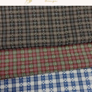 May include: Three folded pieces of fabric featuring a plaid pattern with vertical and horizontal lines. The top fabric is brown and white, the middle is red and green, and the bottom is blue and white. Each piece displays a consistent grid design.