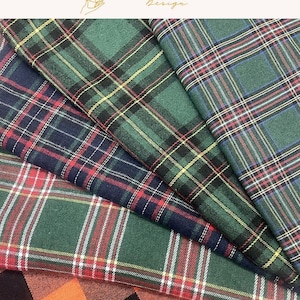May include: A collection of folded fabric swatches featuring various plaid patterns in green, navy blue, red, and white, alongside a piece of orange and black buffalo check fabric. The image includes the text EXPLOREANDSHOP Design.