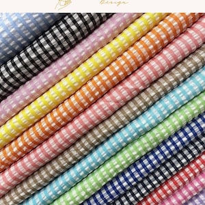 May include: A collection of folded fabric rolls featuring a classic gingham check pattern in various colors including light blue, black, pink, yellow, orange, tan, turquoise, lime green, dark blue, and red, arranged in a diagonal, layered stack.