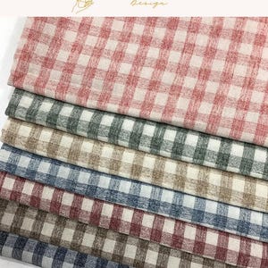 May include: A stack of folded fabric pieces featuring a classic gingham check pattern. The collection includes various colourways such as red, dark green, beige, blue, and brown, all set against a white background with a textured, woven appearance.