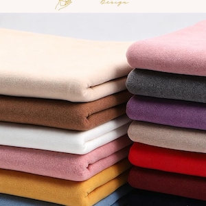 May include: A stack of folded fabric pieces in various solid colors including beige, brown, white, pink, yellow, blue, gray, purple, red, and black. The fabric has a soft, matte, felt-like texture. The text EXPLOREANDSHOP Design is at the top.