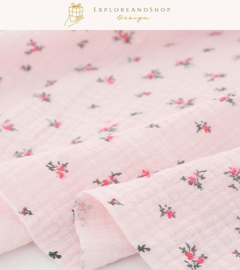 May include: Close-up of a pink fabric with a delicate floral pattern. The fabric is a light pink color with small, scattered red and green floral designs. The fabric is soft and appears to be lightweight, with a slightly wrinkled texture. The text "EXPLOREANDSHOP Design" is in the top right corner.