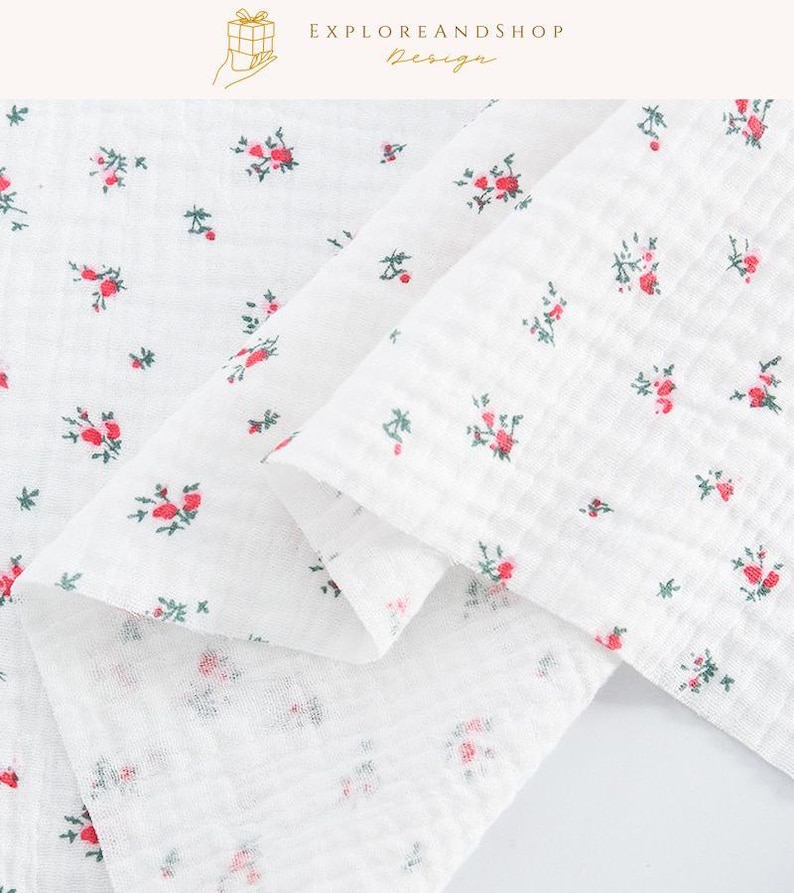 May include: White fabric with a delicate floral pattern featuring small red roses and green leaves. The fabric is folded, showcasing its texture and the scattered floral design. The top right corner has the text "EXPLOREANDSHOP Design."