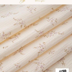 May include: Close-up of a cream-colored fabric with a delicate floral pattern in light purple and brown. The fabric is folded, showing the texture and design. The number "#10" is in the bottom right corner. The top right corner has the text "EXPLOREANDSHOP Design".