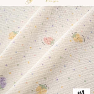 May include: Cream-colored fabric with a repeating pattern of strawberries and colorful polka dots. The strawberries are in various colors, including pink, yellow, and purple. The fabric has a textured appearance. The text "EXPLOREANDSHOP Design" is in the top right corner.
