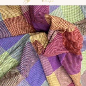 May include: A textile fabric featuring a multi-colored plaid pattern with large squares in shades of yellow, purple, red, and light green. The fabric has a fine grid texture overlaid on the larger blocks of color, creating a complex visual depth.