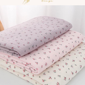 May include: Three folded fabric pieces in shades of lavender, pink, and cream, each adorned with a delicate floral pattern. The fabric is soft and appears to be lightweight, suitable for various crafting projects or home decor.