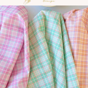 May include: Three folded pieces of fabric featuring a plaid pattern. The left piece is pink and white, the center piece is mint green and white, and the right piece is peach and white. The text EXPLOREANDSHOP Design is visible at the top.