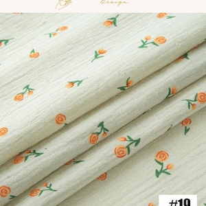May include: Cream-colored fabric with a repeating pattern of orange roses and green leaves. The fabric is folded, showing its texture and design. The text "EXPLOREANDSHOP Design" is at the top, and the number "#19" is in the bottom right corner.