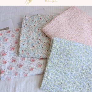May include: Four folded pieces of textured fabric featuring various floral patterns. One piece has pink roses on white, one has small blue and red flowers on white, one has tiny orange flowers on pink, and one has small blue flowers on light green.