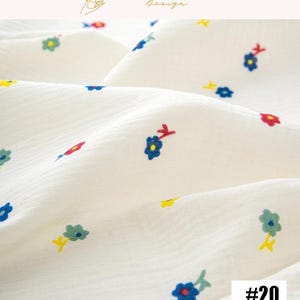May include: Close-up of a white fabric with a textured surface, adorned with small, colorful floral patterns. The flowers are in shades of blue, red, yellow, and green. The number "#20" is visible in the bottom right corner. The top right corner has the text "EXPLOREANDSHOP Design".