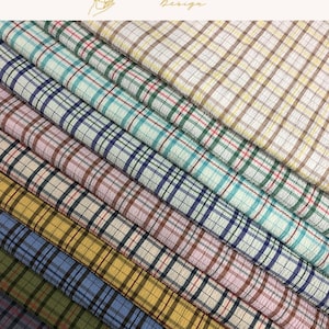May include: A collection of folded fabric bolts featuring a seersucker texture and a consistent plaid pattern. The fabric displays various color combinations including teal, green, pink, brown, yellow, blue, and olive, all with thin dark grid lines.