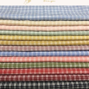 May include: A stack of folded fabric pieces featuring a consistent white grid pattern on various solid colors including light blue, beige, pink, sage green, mustard yellow, mauve, bright blue, coral, olive, red, dark red, and black.