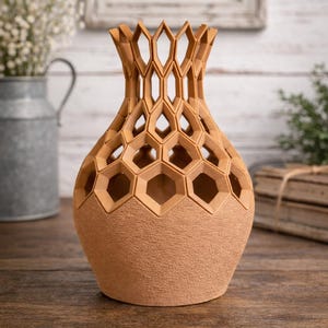 May include: A decorative vase with a unique honeycomb design. The vase is a warm tan color with a textured surface on the lower portion and open hexagonal cutouts on the upper portion. The vase is sitting on a wooden surface.