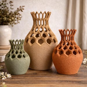 May include: Three decorative vases in varying sizes and colors. The vases have a honeycomb design around the top. The colors are green, tan, and orange. They are displayed on a wooden surface.