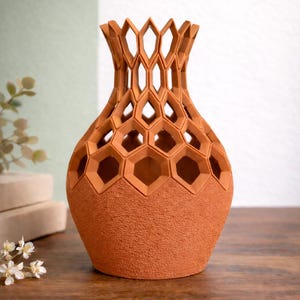 May include: Terracotta-colored vase with a textured surface and a honeycomb design. The vase has a wide base that tapers to a narrower neck with geometric cutouts. The vase is approximately 10 inches tall.