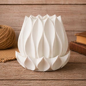 May include: A white, lotus-shaped decorative object. The object is made of a smooth material and features a detailed petal design. The base is a matching lotus shape. The background includes a wooden surface and a ball of twine.