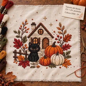 Puede incluir: Un patrón de punto de cruz sobre tela crema con una casa pequeña, un gato negro y calabazas rodeados de hojas otoñales. Una tarjeta indica: Tamaño del diseño: 251 x 251 puntadas Colores DMC: 29. Hilos de bordar y tijeras están cerca.