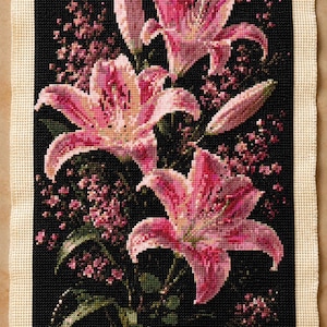 Puede incluir: Una pieza de bordado en punto de cruz rectangular que presenta tres flores de lirio de color rosa vibrante y pequeños racimos de flores rosas sobre un fondo negro sólido, enmarcada por un borde ancho de tela color crema.