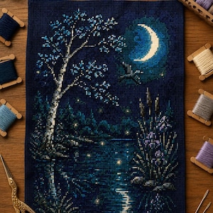 Puede incluir: Un proyecto de bordado en punto de cruz sobre tela azul oscuro que representa un paisaje nocturno con una luna creciente, un árbol y agua. Incluye hilos de bordar en carretes de madera, madejas sueltas y unas tijeras doradas.