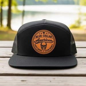 May include: Black trucker hat with a flat brim and mesh back. The hat features a circular patch with the words "BLUE COLLAR AMERICAN" and a skull graphic. The patch is in shades of orange and brown, with the text "DIRTY HANDS CLEAN MONEY".