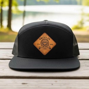 May include: Black trucker hat with a flat brim and mesh back. The front features a brown leather patch with a Native American skull design, the words "Native American", and the years 1776 and 2026.
