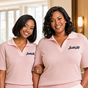 May include: A light pink short-sleeved knit polo shirt with a collar and a V-neckline. The shirt features the text "Jack & Jill" embroidered in dark blue on the left chest. The garment has ribbed cuffs and a ribbed hem at the waist.