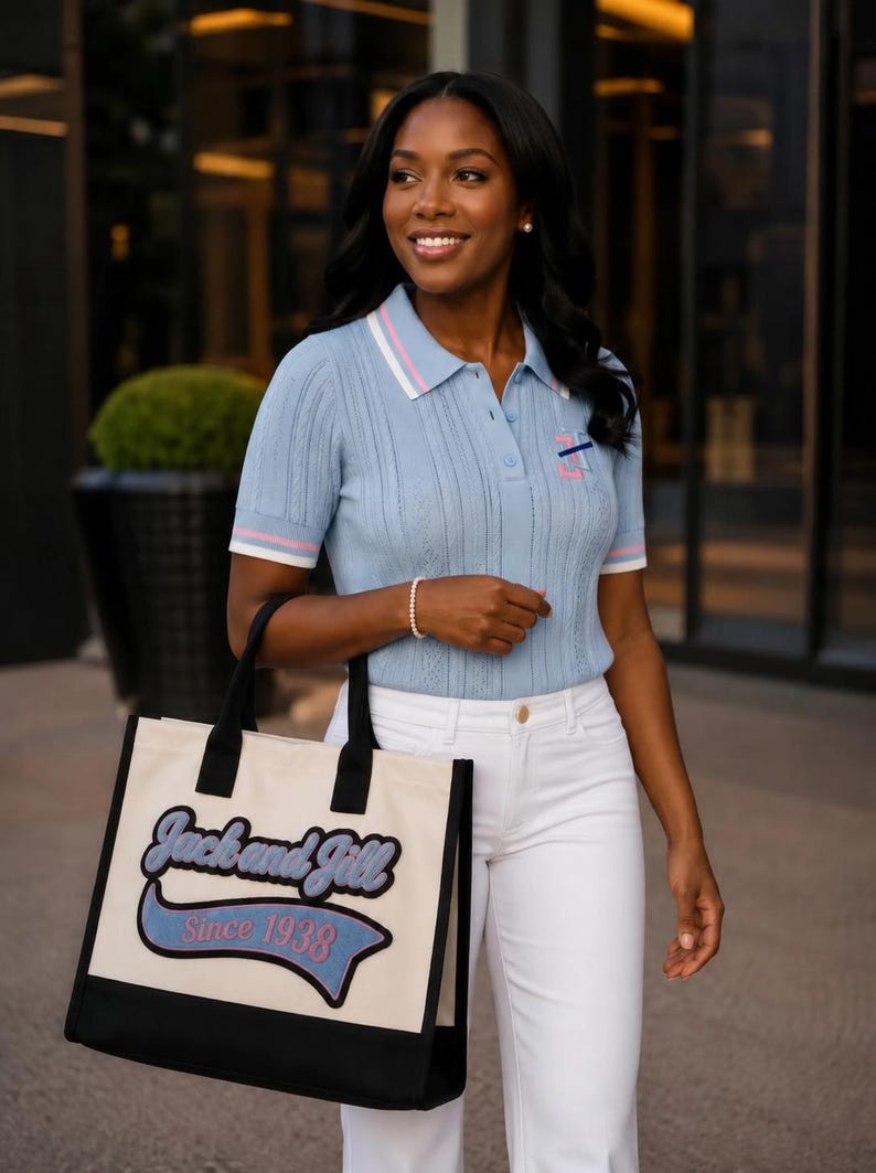 May include: A light blue short-sleeved polo shirt with white and pink striped collar and sleeve cuffs, paired with white pants and a cream-colored canvas tote bag featuring black trim and the text Jack and Jill Since 1938 in blue and pink.