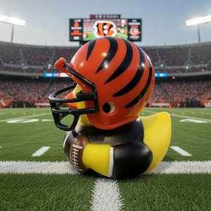 May include: A rubber duck wearing a football helmet with orange and black stripes, and a football. The duck is yellow with black accents, and is on a green football field.