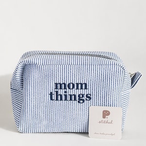 May include: A blue and white striped cosmetic bag with the words "mom things" embroidered on the front. The bag has a zip closure and a small tag that says "stitched".