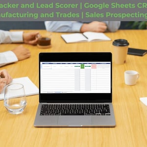 May include: A laptop displaying a spreadsheet is on a wooden table, with people and office supplies around it. The screen shows a data table with green and pink highlighted cells. The text at the top reads "AI B2B Sales Tracker and Lead Scorer".