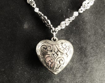 May include: A silver necklace with a heart-shaped pendant. The pendant has an intricate, floral design.