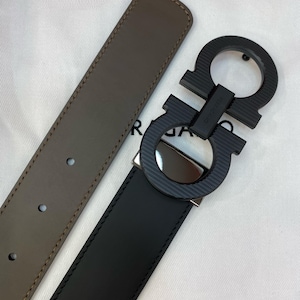 May include: A black and brown leather belt with a black buckle. The buckle features a double Gancini design. The belt is reversible, with a brown side and a black side. The stitching is visible along the edges of the belt.